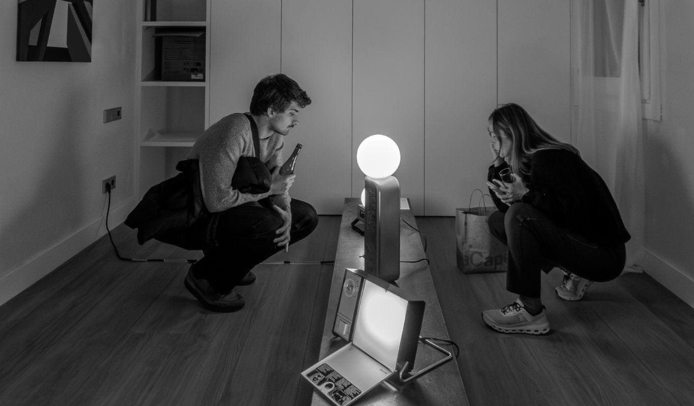 Dos visitantes agachados miran las lámparas de Objectes Perduts en Espai CO38, en blanco y negro